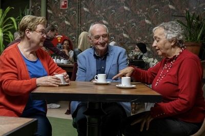 Drie oudere vrienden zitten aan een tafel in een café en genieten van koffie terwijl ze met elkaar praten.