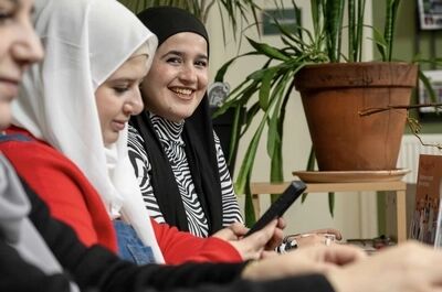 Drie vrouwen, gekleed in verschillende hoofddoeken, zitten aan een tafel en kijken naar hun telefoons.