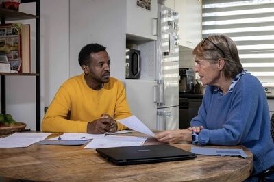 Twee volwassenen in gesprek aan een tafel, met documenten en een laptop voor hen.